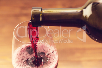 Pouring red wine into the glass against wooden background