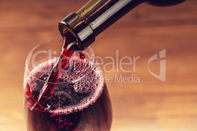 Pouring red wine into the glass against wooden background