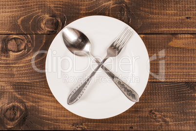 Empty white plate with silverware on wooden table. View from above