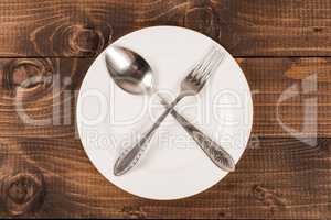 Empty white plate with silverware on wooden table. View from above