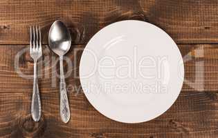 Empty white plate with silverware on wooden table. View from above