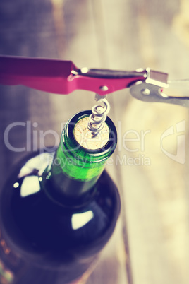 Bottle of wine with corkscrew on wooden background