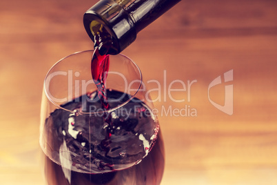 Pouring red wine into the glass against wooden background