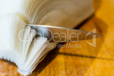 Macro of pointy knife cutting white onion layers