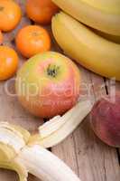 Bananas apple mandarin peach on wooden background as health food concept