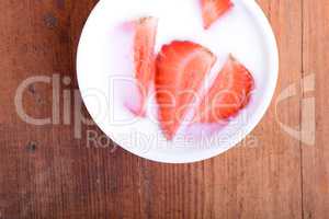 Slice of pie with strawberry on white plate, milk drink, wooden background. Top view
