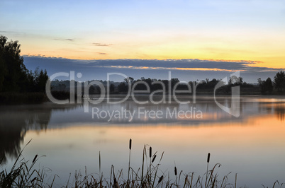 The morning landscape with sunrise over water in the fog