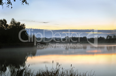 The morning landscape with sunrise over water in the fog