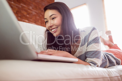 Smiling asian woman on couch using laptop