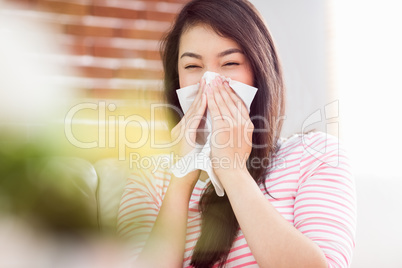 Asian woman blowing her nose on couch
