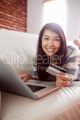 Smiling asian woman on couch using laptop to shop online