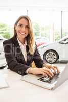 Smiling saleswoman typing on her laptop