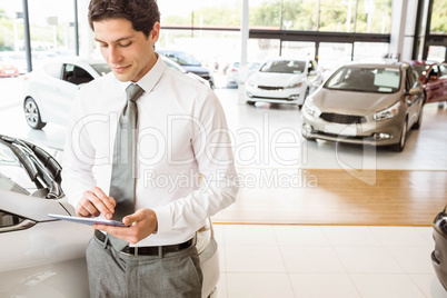 Smiling salesman using tablet near a car