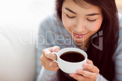 Asian woman relaxing on couch with coffee