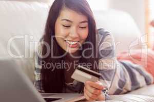 Smiling asian woman on couch using tablet to shop online