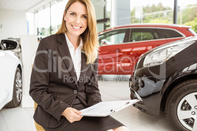 Smiling saleswoman sitting near cars