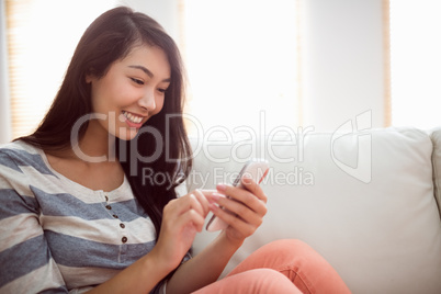 Smiling asian woman on couch using phone