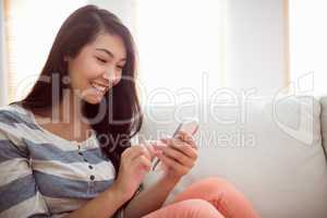 Smiling asian woman on couch using phone