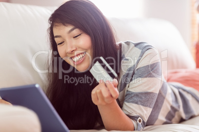 Smiling asian woman on couch using tablet to shop online