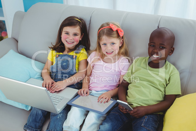 Happy kids sitting together with a tablet and laptop and phone