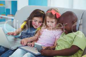 Happy kids sitting together with a tablet and laptop and phone