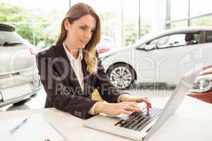 Smiling saleswoman typing on her laptop