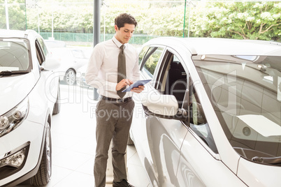 Smiling salesman using tablet near a car