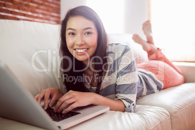 Smiling asian woman on couch using laptop