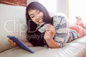 Smiling asian woman on couch using tablet to shop online