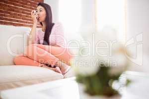 Asian woman using her inhaler on couch