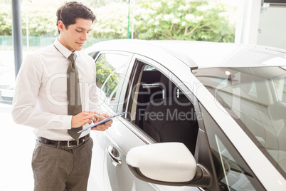 Smiling salesman using tablet near a car