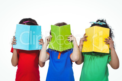 Three kids standing with books in front of their faces