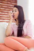 Asian woman using her inhaler on couch