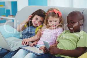 Happy kids sitting together with a tablet and laptop and phone