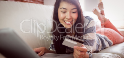 Smiling asian woman on couch using tablet to shop online