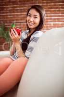 Smiling asian woman on couch having hot drink