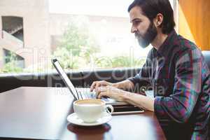 Hipster student using laptop in canteen