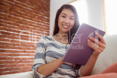 Smiling asian woman using tablet on couch