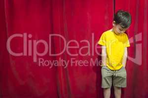 Pouting Mixed Race Boy Standing In Front of Red Curtain