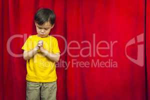 Mixed Race Boy Praying in Front of Red Curtain