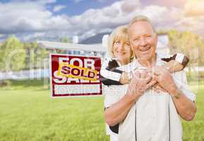 Senior Couple in Front of Sold Real Estate Sign and House