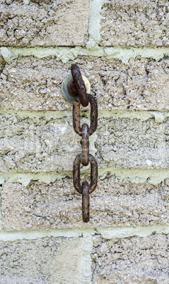 Short rusted chain handing from brick wall