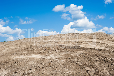 Sandy dirt hill with tracks against clouds and sky