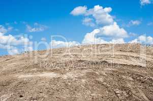 Sandy dirt hill with tracks against clouds and sky