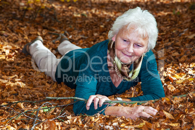 Senior woman lying in autumn leaves in the park