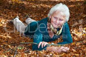 Senior woman lying in autumn leaves in the park