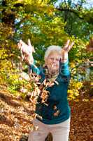 Senior woman poses with autumn leaves in the park