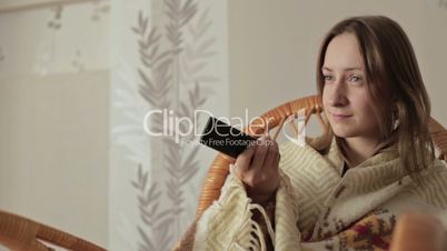 Young woman covered with blanket holding remote control and watching tv at home
