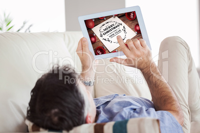 Composite image of man laying on sofa using a tablet pc