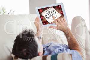 Composite image of man laying on sofa using a tablet pc
